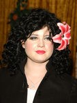 Kelly Osbourne con melena ondulada negra y tocado de flor 