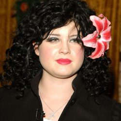 Kelly Osbourne con melena ondulada negra y tocado de flor 